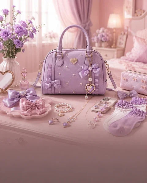 A pastel lavender quilted handbag with pearl embellishments, bow details, and a dangling heart charm, displayed on a pink bed in a bedroom setting alongside matching accessories.